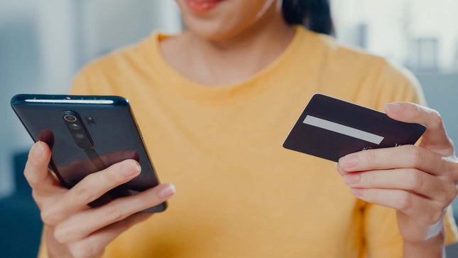 Photo shows a woman using a credit card to make purchases on her phone. 